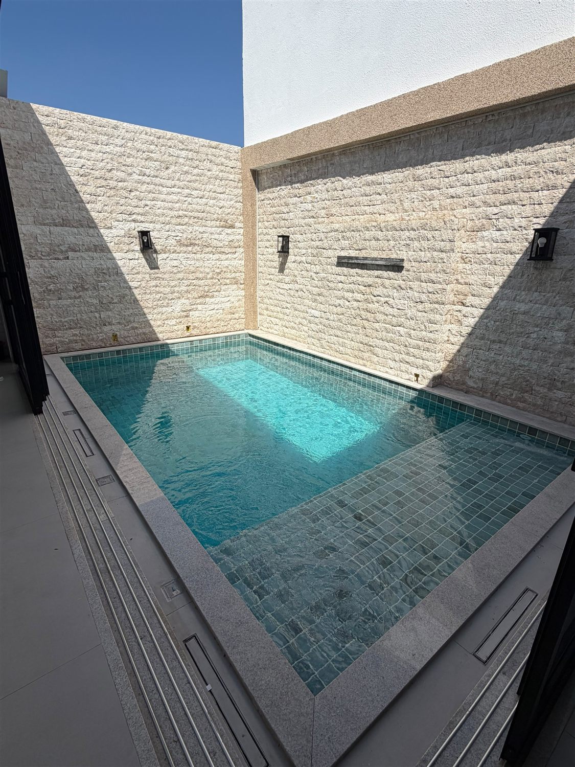 Piscina de azulejo verde-água cercada por parede de pedra
