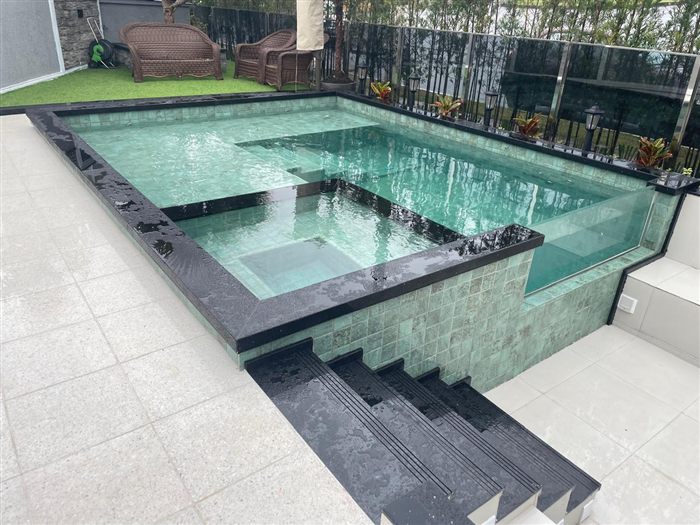 Piscina com borda de vidro e revestimento cerâmico, com degraus em pedra escura